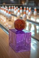 A vivid bowling ball perched atop a purple cube in a lively bowling alley during the evening photo