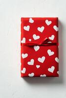 A beautifully wrapped red gift box adorned with white heart patterns on a simple background photo