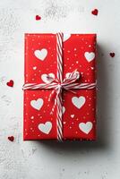 A beautifully wrapped red gift box adorned with white heart patterns on a simple background photo