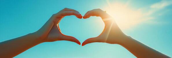 A hand forms a heart shape against the backdrop of a sunset over the ocean photo