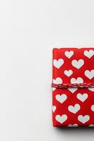 A beautifully wrapped red gift box adorned with white heart patterns on a simple background photo