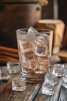 A glass filled with ice cubes on a wooden table illuminated by warm sunlight in the afternoon photo