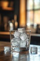 A glass filled with ice cubes on a wooden table illuminated by warm sunlight in the afternoon photo