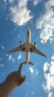 A person reaching towards a plane flying high in a clear blue sky on a sunny day photo