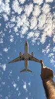 un persona alcanzando hacia un avión volador alto en un claro azul cielo en un soleado día foto