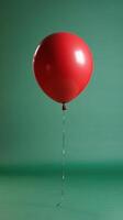 A single red balloon floats gracefully against a simple green backdrop in a quiet indoor setting photo
