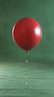 A single red balloon floats gracefully against a simple green backdrop in a quiet indoor setting photo