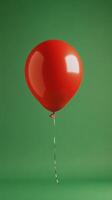 A single red balloon floats gracefully against a simple green backdrop in a quiet indoor setting photo