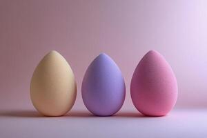 Three pastel beauty blending sponges arranged on a soft pink surface with gentle light photo