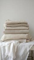 Soft, neatly folded cream colored blankets on a light surface by a neutral backdrop photo