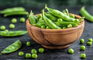 Freshly harvested green peas in a wooden bowl with scattered pods and peas on a dark surface photo