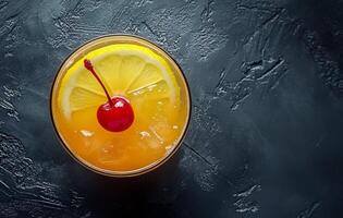 Refreshing orange cocktail topped with a cherry and lemon slice on a dark surface photo