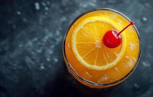 Refreshing orange cocktail topped with a cherry and lemon slice on a dark surface photo
