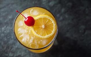 Refreshing orange cocktail topped with a cherry and lemon slice on a dark surface photo