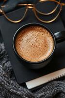 Morning coffee in a cozy workspace with glasses and a notebook on a black table photo