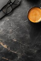 Morning coffee in a cozy workspace with glasses and a notebook on a black table photo