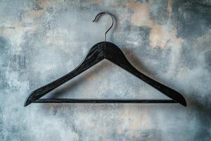 A simple black wooden hanger against a textured gray wall in a minimalist setting photo