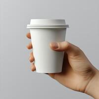A person holds a plain white coffee cup with a black lid against a grey background photo
