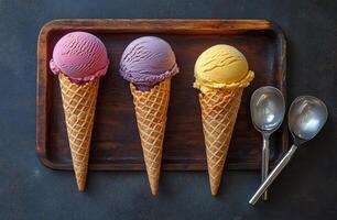 Three colorful ice cream scoops served in a waffle cone on a wooden platter with spoons photo