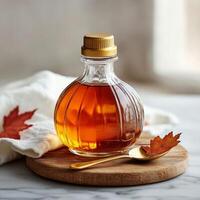 A glass bottle of maple syrup on a wooden board with autumn leaves and a golden spoon photo