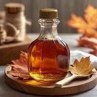 A glass bottle of maple syrup on a wooden board with autumn leaves and a golden spoon photo