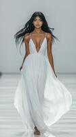 A model walks confidently in a flowing white gown, showcasing elegance and grace in soft lighting photo
