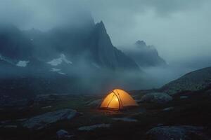 A solitary tent glows warmly in a misty mountain landscape during twilight hours photo