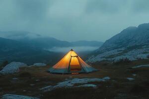 A solitary tent glows warmly in a misty mountain landscape during twilight hours photo