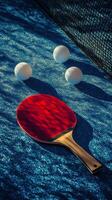 A red table tennis paddle rests on a blue surface alongside three white balls during daylight photo