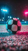 A vibrant soccer ball rests on the ground under colorful stadium lights at night photo