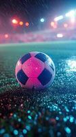 A vibrant soccer ball rests on the ground under colorful stadium lights at night photo