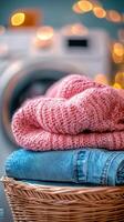 Soft knit sweaters and denim stacked in a wicker basket near a washing machine with flowers photo