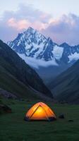 A cozy tent glows warmly in the mountains at dusk surrounded by misty peaks photo