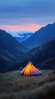 A cozy tent glows warmly in the mountains at dusk surrounded by misty peaks photo