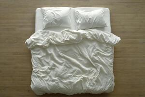 Comfortable unmade bed with white linens and pillows on wooden floor in a bright room photo