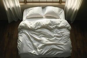 Comfortable unmade bed with white linens and pillows on wooden floor in a bright room photo