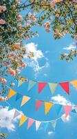 Colorful bunting flags hanging under lush green trees against a vibrant blue sky photo
