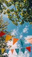 Colorful bunting flags hanging under lush green trees against a vibrant blue sky photo