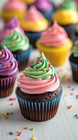 Colorful cupcakes with swirl frosting and sprinkles displayed on a white wooden table photo
