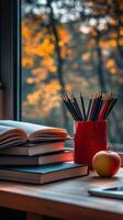 A cozy study corner featuring books, stationery, and a red apple next to the window on a rainy day photo