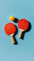 Two red table tennis paddles and a yellow ball on a blue background in a minimalistic arrangement photo