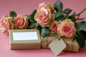 Gift box and pink roses arranged on a pink background with a blank card for writing messages photo