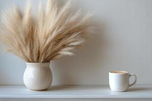 Soft pampas grass arrangement in a minimalist setting beside a cozy cup on a shelf photo