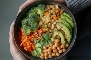 Healthy vegetarian bowl featuring fresh vegetables, chickpeas, and avocado held by hands photo