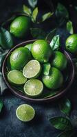 Fresh limes and lime halves arranged in a bowl with green leaves on a dark background photo