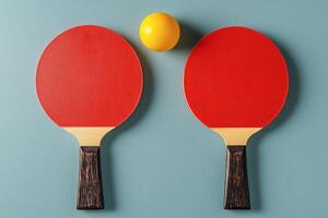 Two red table tennis paddles and a yellow ball on a light blue background photo