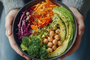 Healthy vegetarian bowl featuring fresh vegetables, chickpeas, and avocado held by hands photo