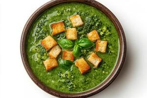 A bowl of creamy broccoli soup topped with croutons and fresh basil leaves photo