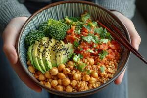 Healthy vegetarian bowl featuring fresh vegetables, chickpeas, and avocado held by hands photo