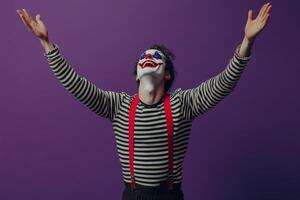 A performer dressed as a clown presents an entertaining act against a vibrant purple backdrop photo